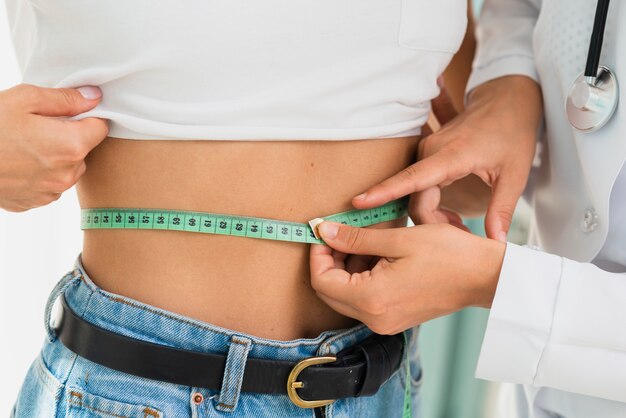 Doctor measuring a woman's waistline with a tape measure during a weight loss consultation with Ozempic guidance.